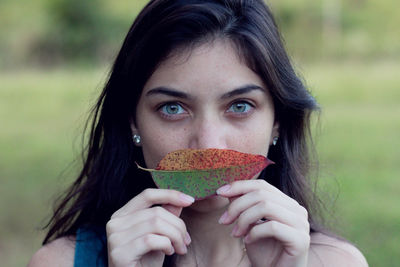 Portrait of young woman holding leaf while standing outdoors