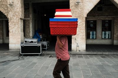 Side view of man carrying plastic crates against building