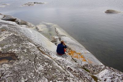 Rear view of man sitting on rocky shore