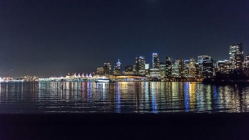 Illuminated buildings by sea against clear sky at night