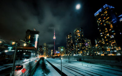 Illuminated railroad tracks amidst buildings in city at night