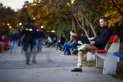 Full length of man using laptop while sitting on bench at public park