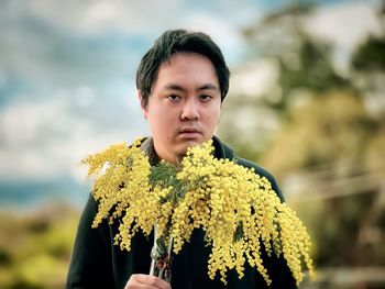 Portrait of young man standing against yellow flowering plants