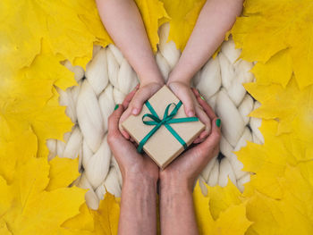 Cropped hands of mother and daughter holding gift on autumn leaves