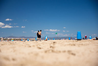 Rear view of men on beach against blue sky