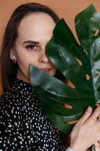 Woman in polka dot dress covers half of her face with a petal of a tropical plant 