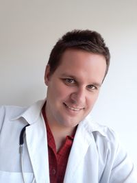 Portrait of male doctor standing against wall at home