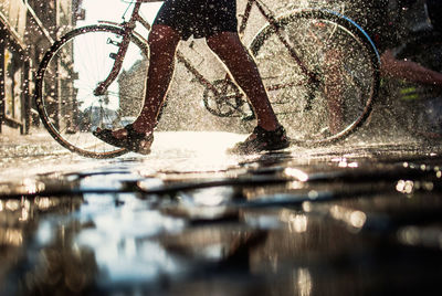Low section of man walking with bicycle on puddle in street
