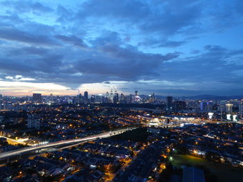 High angle view of city lit up against cloudy sky