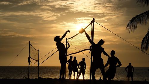 Silhouette people playing volleyball at beach against cloudy sky during sunset