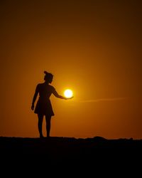 Silhouette woman standing on field against sky during sunset