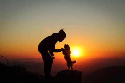 Silhouette men standing on shore against sky during sunset