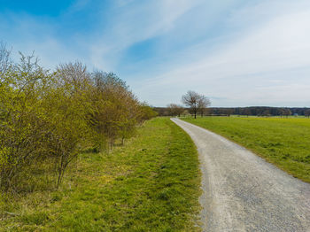 Empty road amidst field against sky