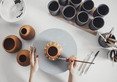 Cropped hands of potter painting ceramics on table in workshop