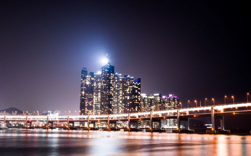 Illuminated bridge over river against buildings