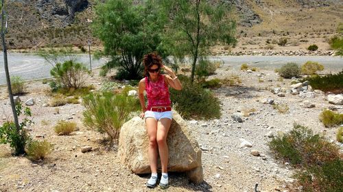 Full length of woman sitting on rock against trees