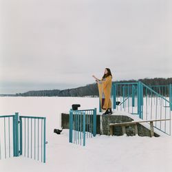 Man standing on railing against snowcapped mountain during winter
