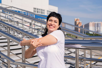 Portrait of smiling young woman standing against railing in city