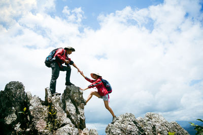 Low angle view of man climbing on rock against sky