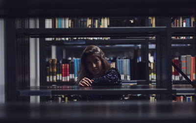 Portrait of young woman seen through bookshelves at library