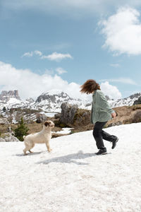 Side view of unrecognizable female playing with spanish water dog on snowy lawn in dolomites while having fun on sunny day in winter