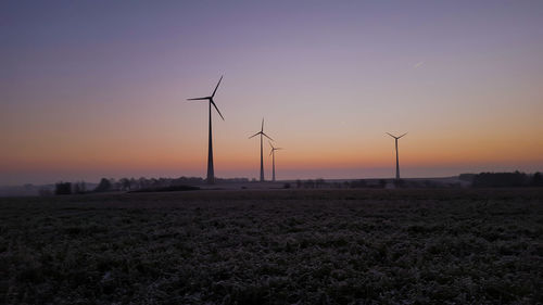 Windmills on field against clear sky at dusk