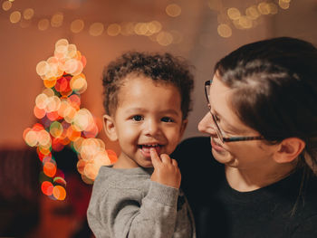 Close-up of mother with cute son against illuminated christmas lights at home