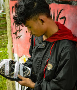 Young man looking at mask while standing outdoors