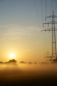 Electricity pylon on landscape against sky during sunset