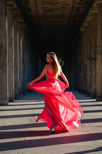 Full length rear view of young woman in pink evening gown dancing at colonnade