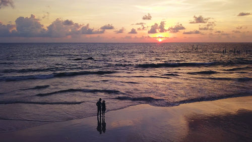 Rear view of silhouette couple on shore at beach during sunset