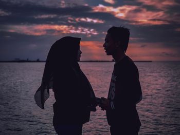 Rear view of couple standing on beach during sunset