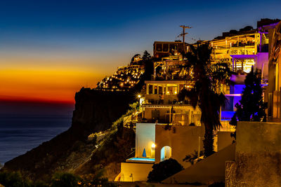 Illuminated buildings by sea against sky at sunset