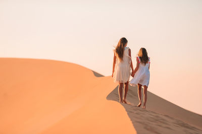 Rear view of women walking on sand dune