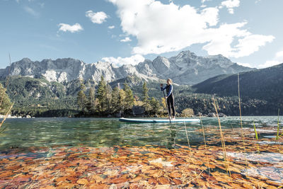 Germany, bavaria, garmisch partenkirchen, young woman stand up paddling on lake eibsee