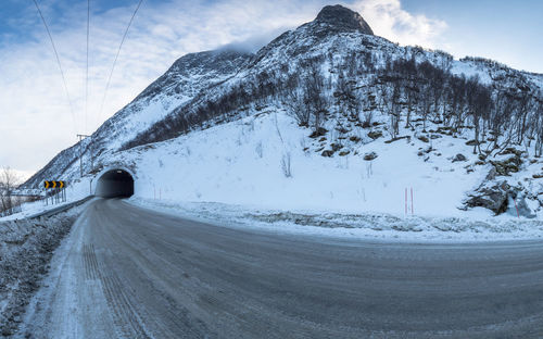 Road leading towards tunnel against snowcapped mountains