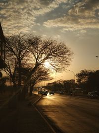 Road by trees against sky during sunset in city