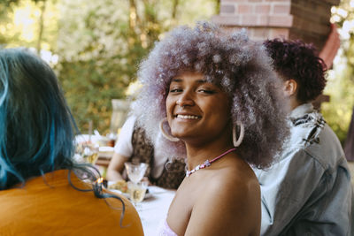 Side view portrait of smiling transwoman with curly hair during dinner party in back yard