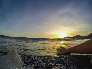 Low section of woman on beach against sky during sunset