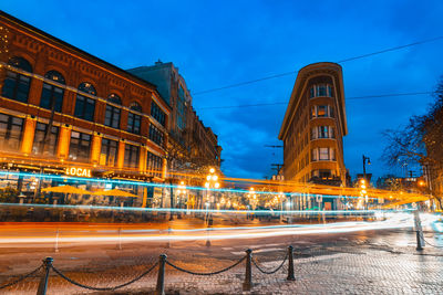 Light trails on road by building against sky at night