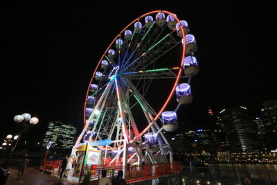 Low angle view of illuminated ferris wheel against buildings at night