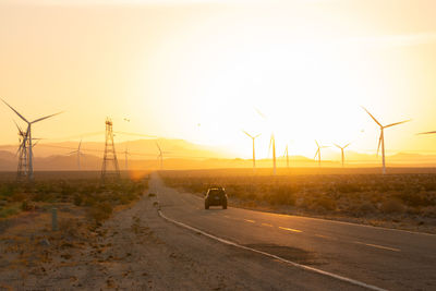 Wind turbines on road against sky during sunset