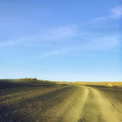 Dirt road amidst field against blue sky