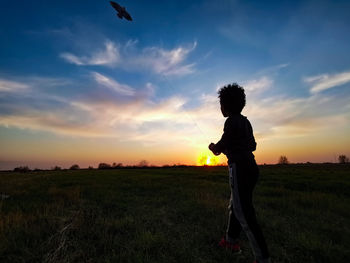 Silhouette man standing on field against sky during sunset