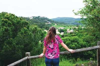 Rear view of woman standing by railing against trees