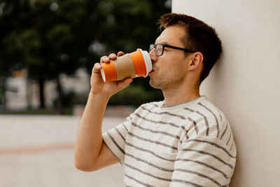 Young adult man sitting outdoors, drinking coffee, enjoying good weather and city view. 