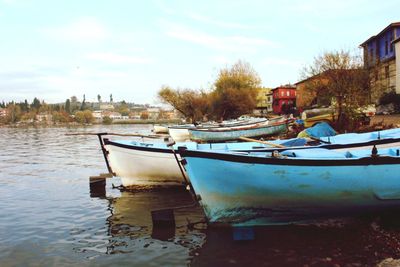 Boat moored on shore in city against sky