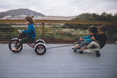 Boy pulling toy car with friends while riding tricycle on floorboard