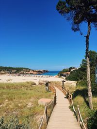 Footpath by sea against clear blue sky