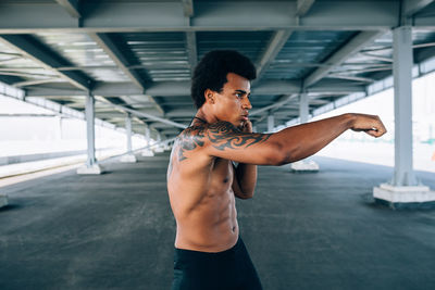 Shirtless male boxer exercising below bridge